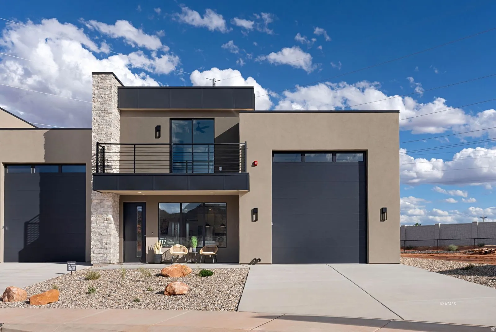 Contemporary stucco exterior featuring a stone facade accent, a second-story balcony with metal railings, and a two-car garage with modern doors