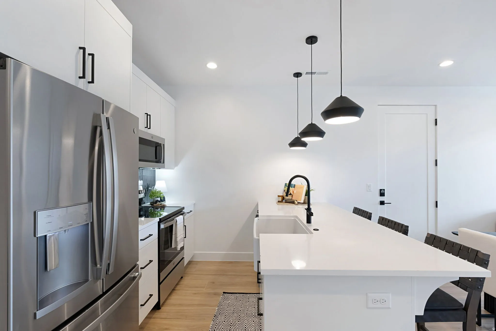 Modern kitchen featuring stainless steel appliances, white cabinetry with matte black hardware, recessed lighting, and wood-finish flooring
