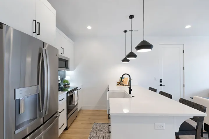 Modern kitchen featuring stainless steel appliances, white cabinetry with matte black hardware, recessed lighting, and wood-finish flooring