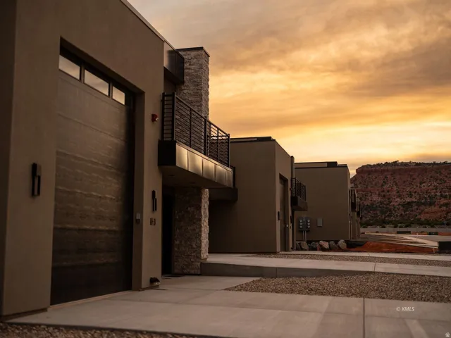 Modern stucco exterior with a wood-grain garage door, stone accents, and a private balcony with black railings