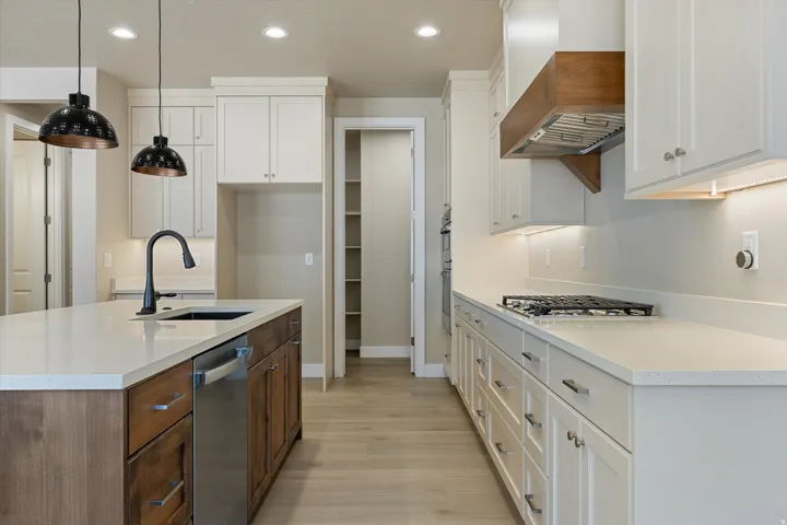 Gourmet kitchen featuring a central island with an undermount sink, light-toned countertops, white cabinetry with contemporary hardware, a built-in gas cooktop, and a custom wood-hood range vent
