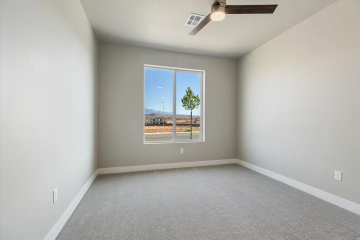 Neutral-toned room featuring a large window, light gray carpeting, and a ceiling fan with integrated lighting