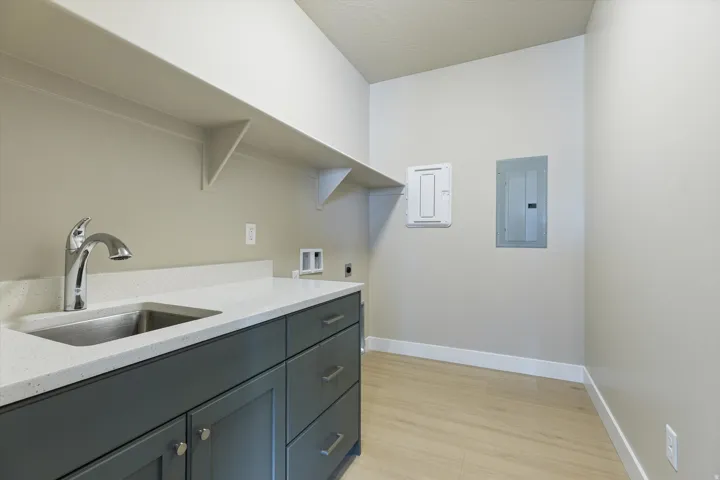Utility room featuring a stainless steel sink, chrome faucet, white countertop, dark cabinetry, and wood-finish flooring