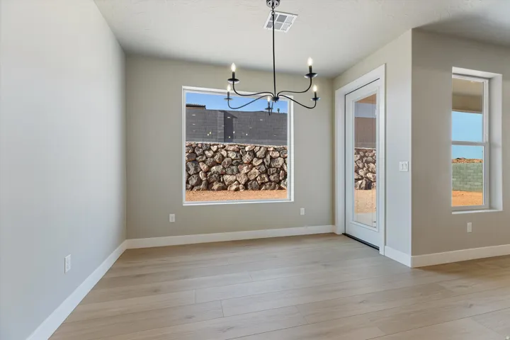 Open-concept room featuring light wood-finish flooring, a contemporary chandelier, multiple windows, and a glass-paneled door