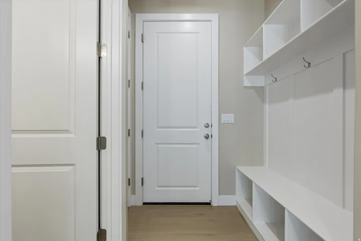 Entryway featuring integrated white storage bench with cubbies, white wall paneling, and an upper shelf with coat hooks