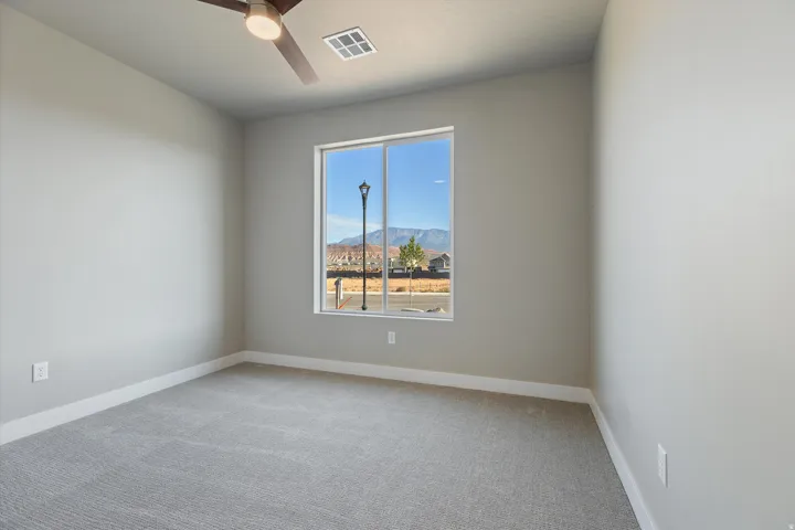 Carpeted room featuring a large window, neutral wall paint, white trim, and a ceiling fan with integrated lighting