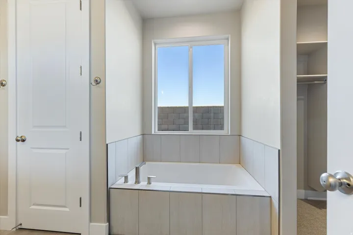 Soaking tub with a tiled surround, featuring a window and contemporary fixtures