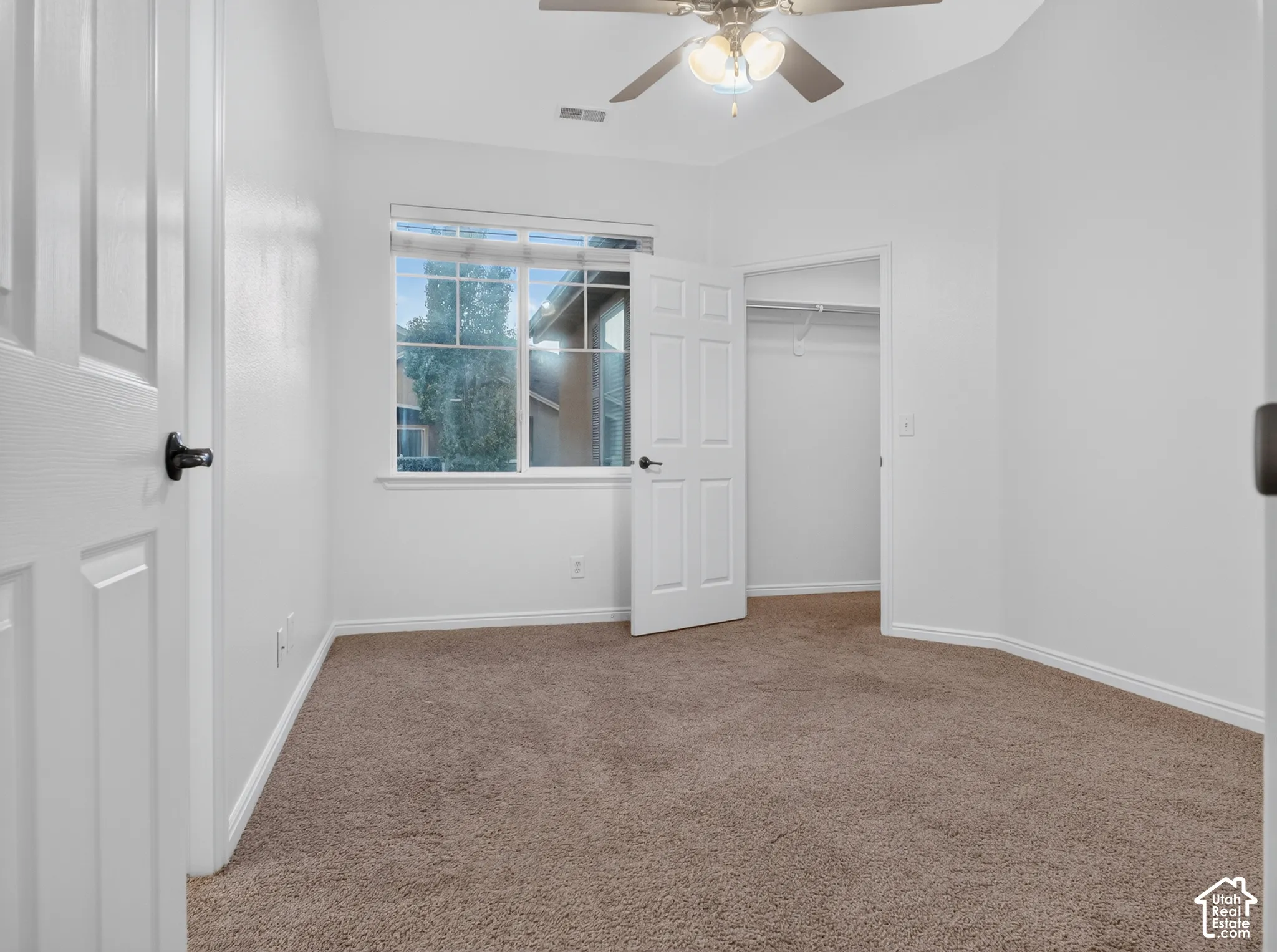Room featuring neutral-toned carpeting, white walls, a multi-pane window, and a ceiling fan with integrated lighting