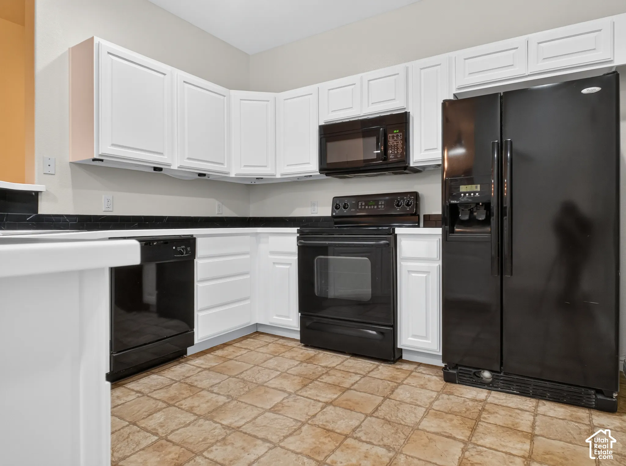 White cabinetry with black countertops, black appliances, and neutral tile flooring