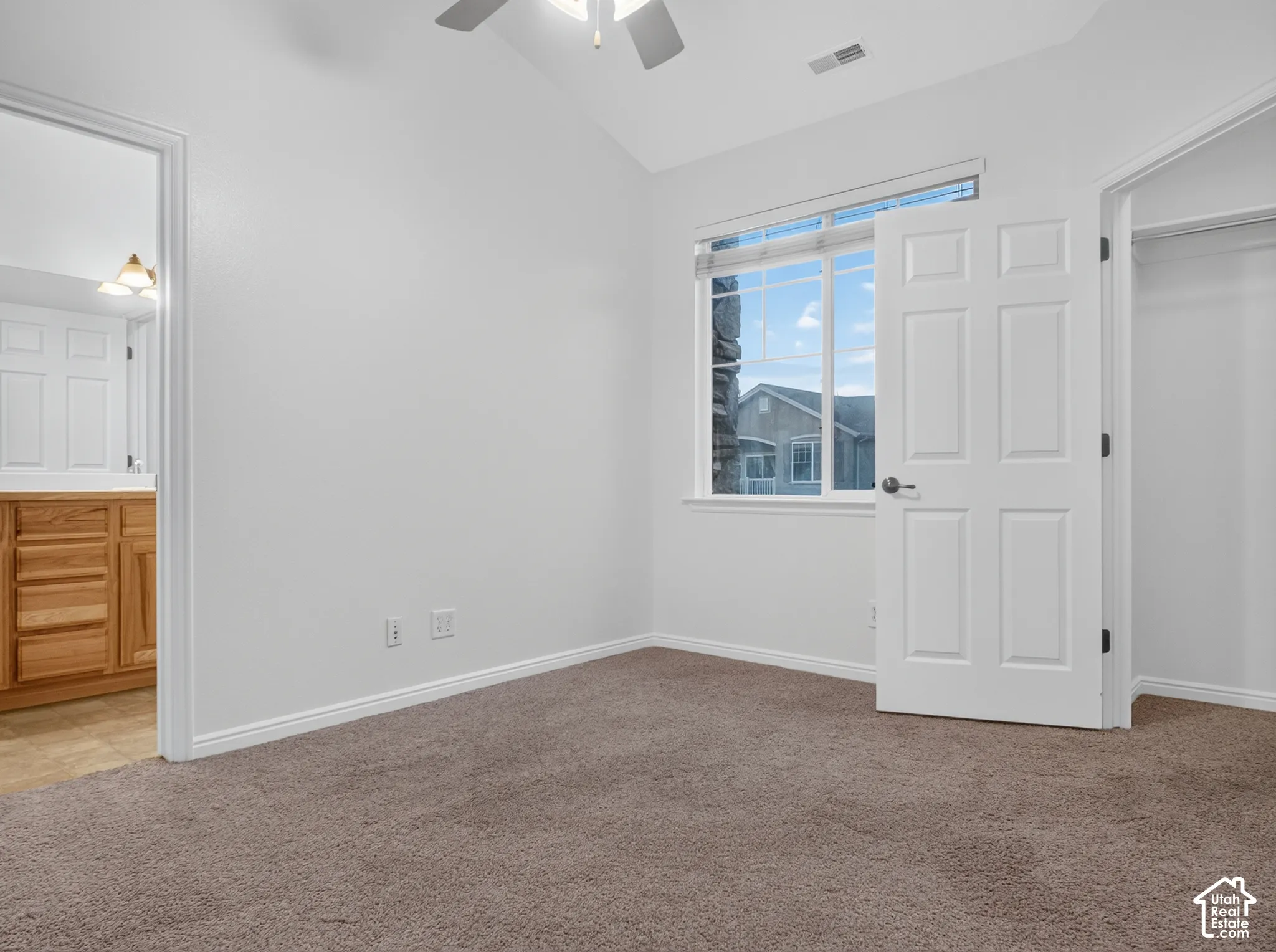 Vaulted ceiling with an attached ceiling fan, large window, broadloom carpeting, and a closet with a built-in hanging rod