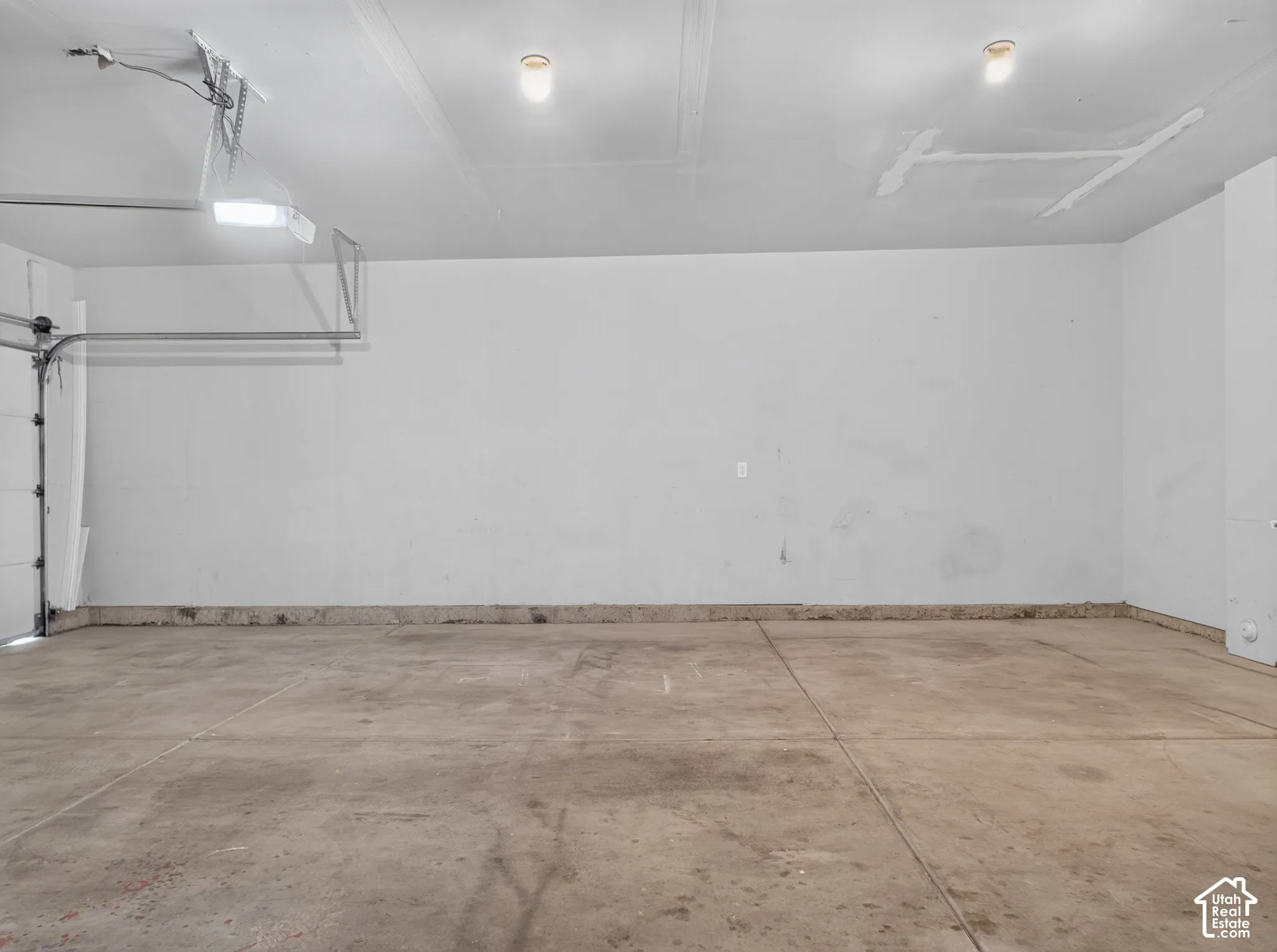 Attached garage with concrete flooring, wall-mounted lighting, and an overhead garage door mechanism