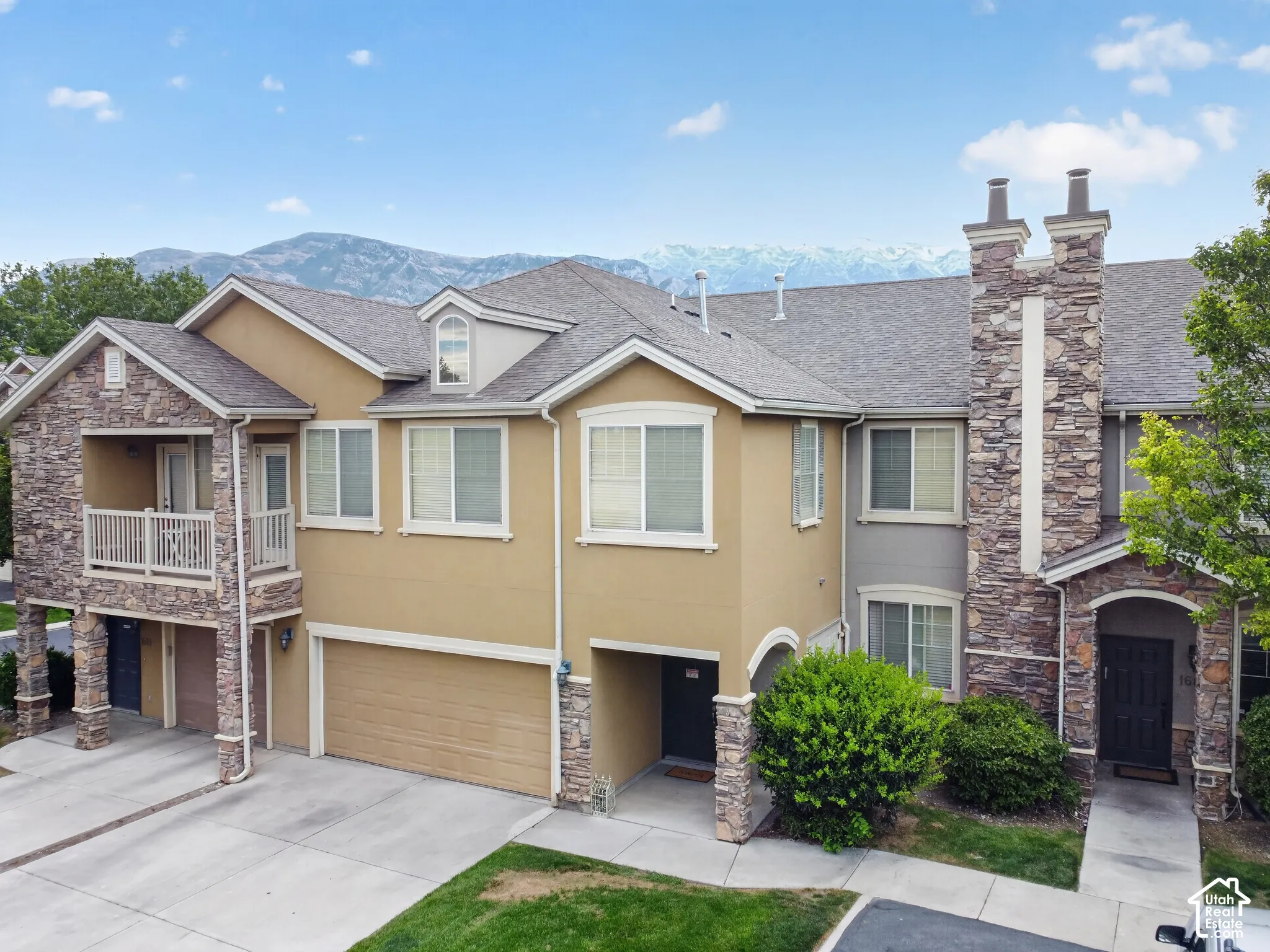 Multi-level residence featuring a stone and stucco exterior, prominent two-car garage, and a second-story balcony