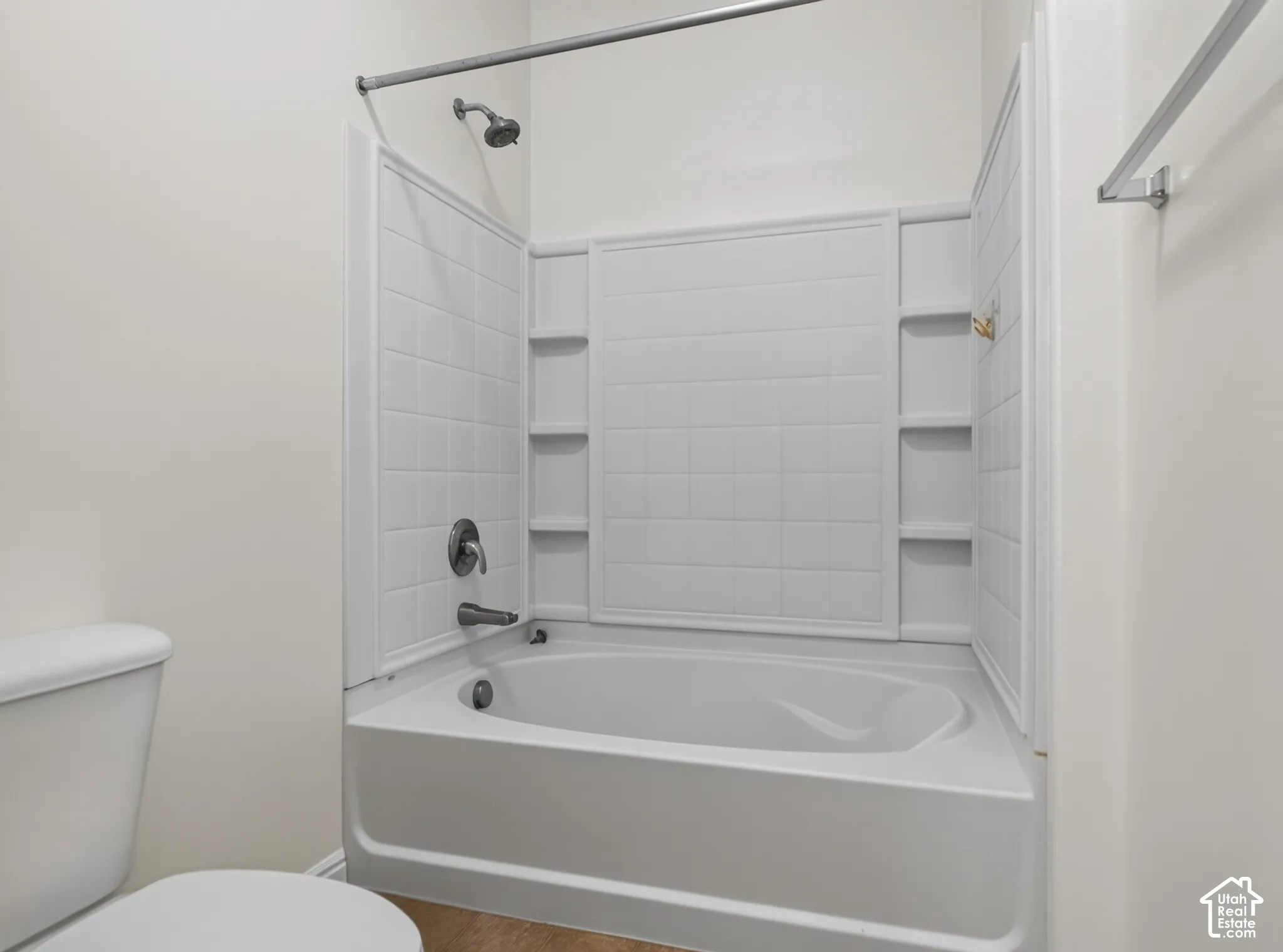 White bathtub with integrated shower, chrome fixtures, and built-in shelving