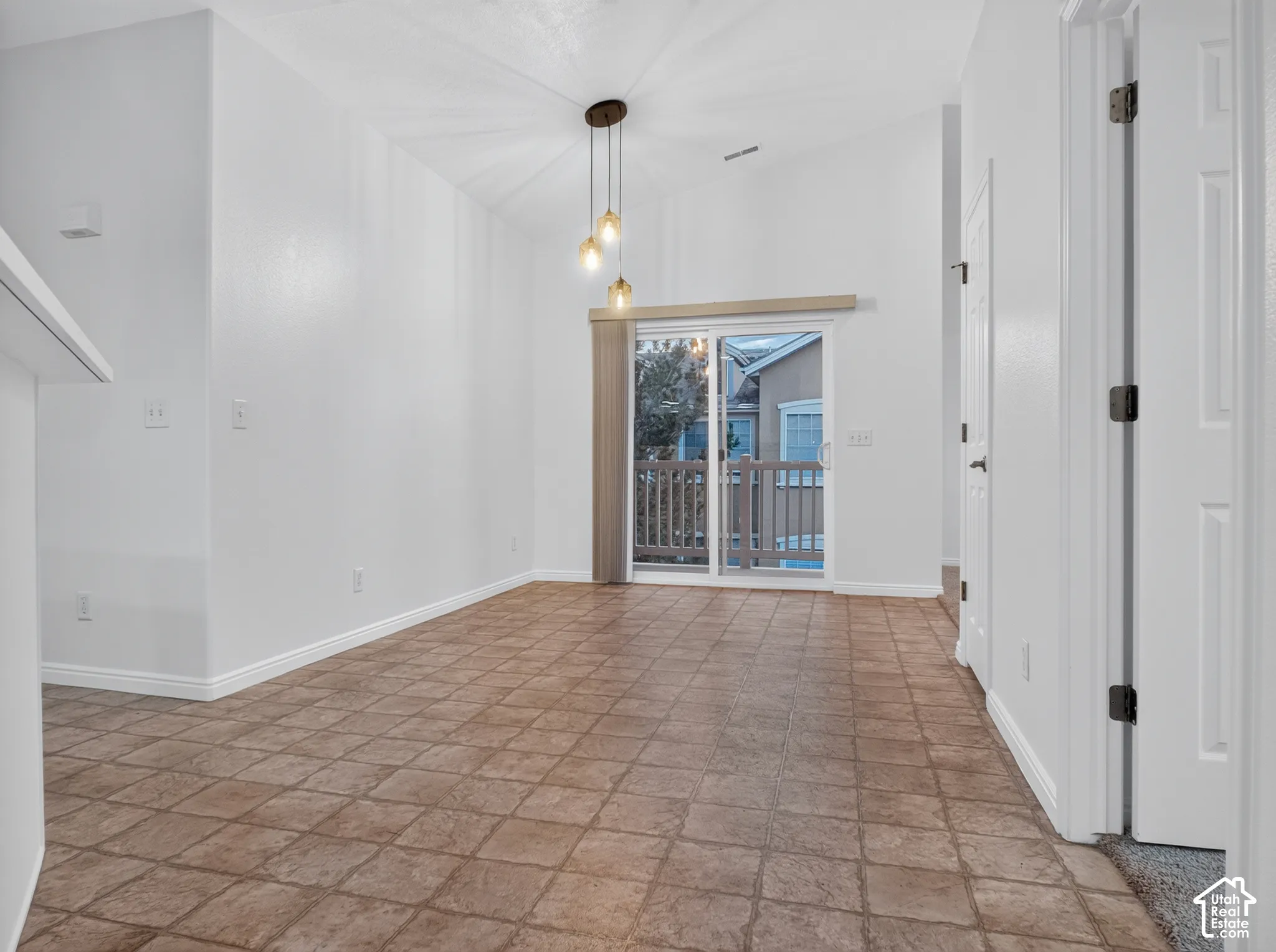Vaulted ceiling with pendant lighting, sliding glass door to exterior, and tiled flooring