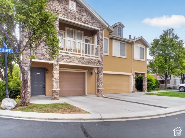 Multi-level residence featuring stone and stucco exterior, an attached garage, and a balcony with white railings