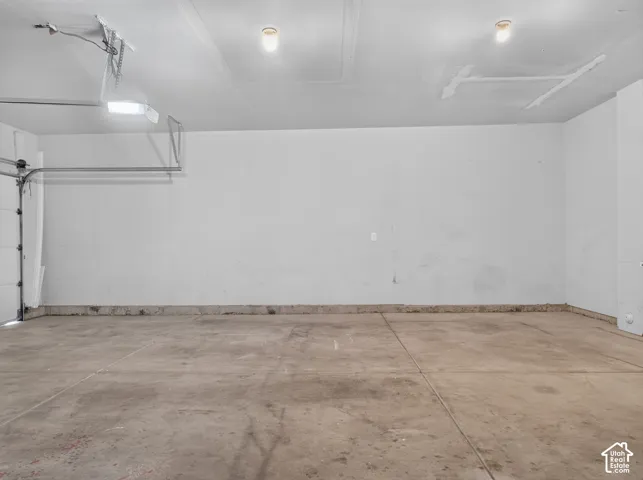 Attached garage with concrete flooring, wall-mounted lighting, and an overhead garage door mechanism