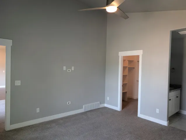 Carpeted room with high ceilings, featuring a ceiling fan with integrated lighting, a walk-in closet with built-in shelving, and an en-suite vanity with a countertop and cabinetry