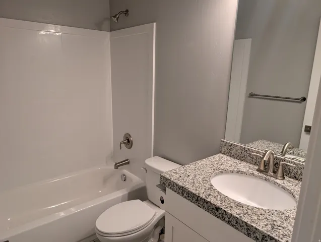 Bathroom featuring a white bathtub with a shower combination, brushed nickel fixtures, a white toilet, a vanity with a granite countertop and an undermount sink, and a large mirror