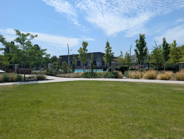 Expansive green lawn area featuring a paved pathway, mature trees, and landscaping