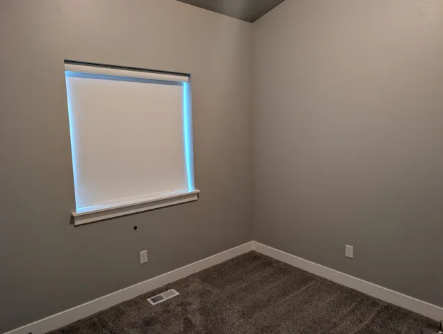 Neutral wall paint and plush carpet flooring define this room, featuring a window with a roller shade and white trim