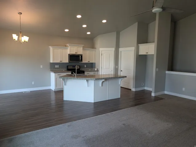 Open-concept kitchen featuring white cabinetry, granite countertops, a central island with integrated sink, stainless steel appliances, and recessed lighting