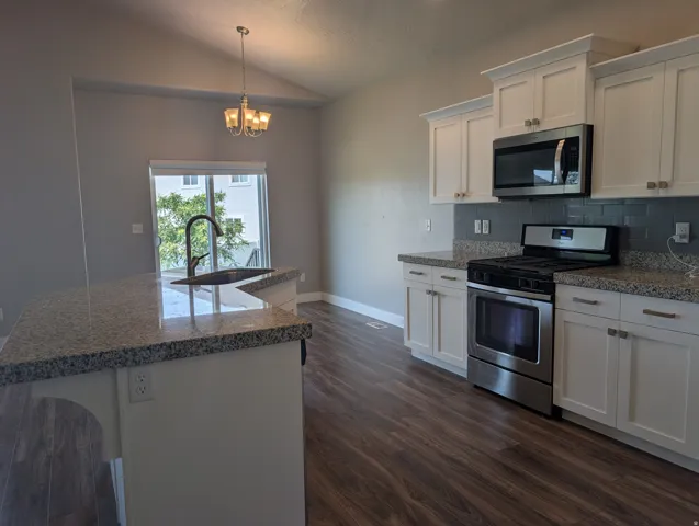 Contemporary kitchen featuring white shaker cabinetry, speckled countertops, stainless steel appliances, and wood-finish flooring