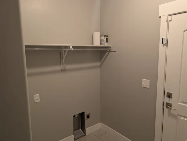 Dedicated utility space featuring a wall-mounted shelf, clothes hanging rod, and tile flooring