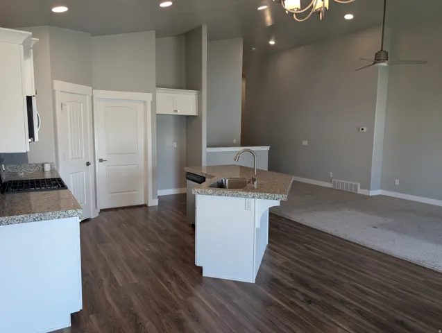 Kitchen island with integrated stainless steel sink and gooseneck faucet, granite countertops, wood-finish flooring, white cabinetry, and recessed lighting