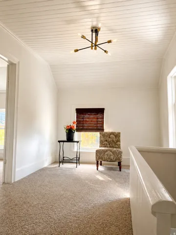 Carpeted flooring, window with natural light, white painted walls, white shiplap ceiling, and a modern light fixture
