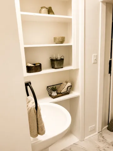 Built-in shelving, white walls, white porcelain basin, black towel ring, and patterned tile flooring