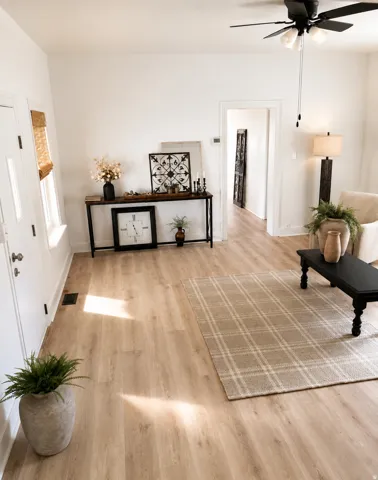 Light wood-finish flooring, white walls, and a black ceiling fan with integrated lighting