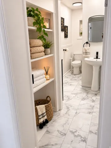 Built-in shelving, pedestal sink, wall-mounted mirror, recessed shelving niche, and tiled flooring with a marble-effect finish