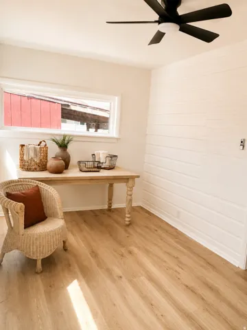 Wood-finish flooring with a white shiplap accent wall, overhead ceiling fan, and a single horizontal window