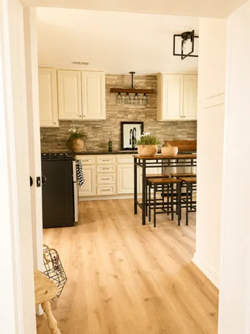 Kitchen featuring wood-finish flooring, stone-finish backsplash, cream cabinetry, dark countertops, and a black appliance