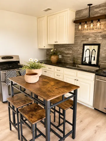 Kitchen featuring wood-finish flooring, white cabinetry, dark countertops, a stacked stone backsplash, and stainless steel appliances