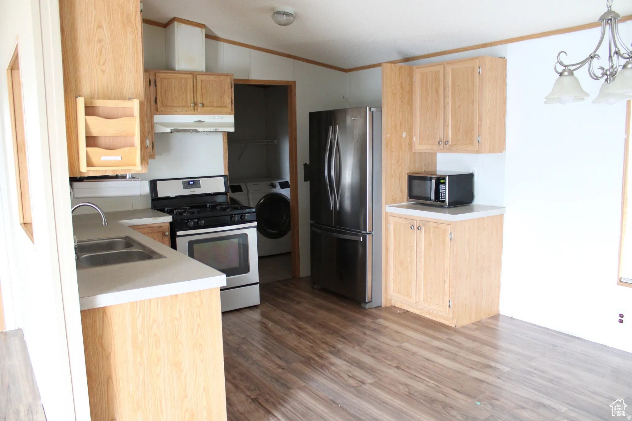 Kitchen featuring wood-finish flooring, light wood cabinetry, stainless steel appliances, and a double basin sink