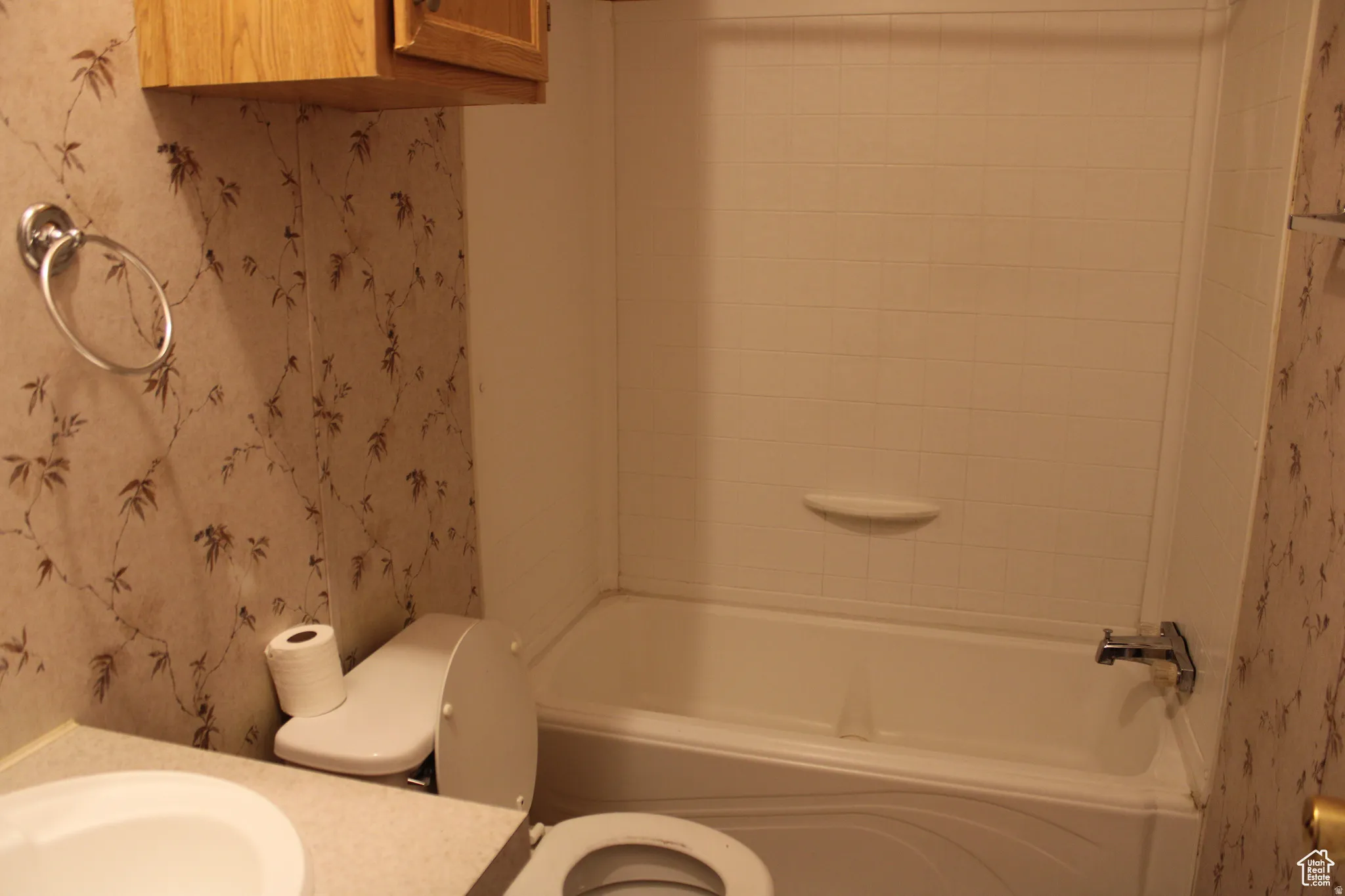 Full bathroom featuring a white bathtub with a tiled surround, a toilet, and a vanity with an integrated sink