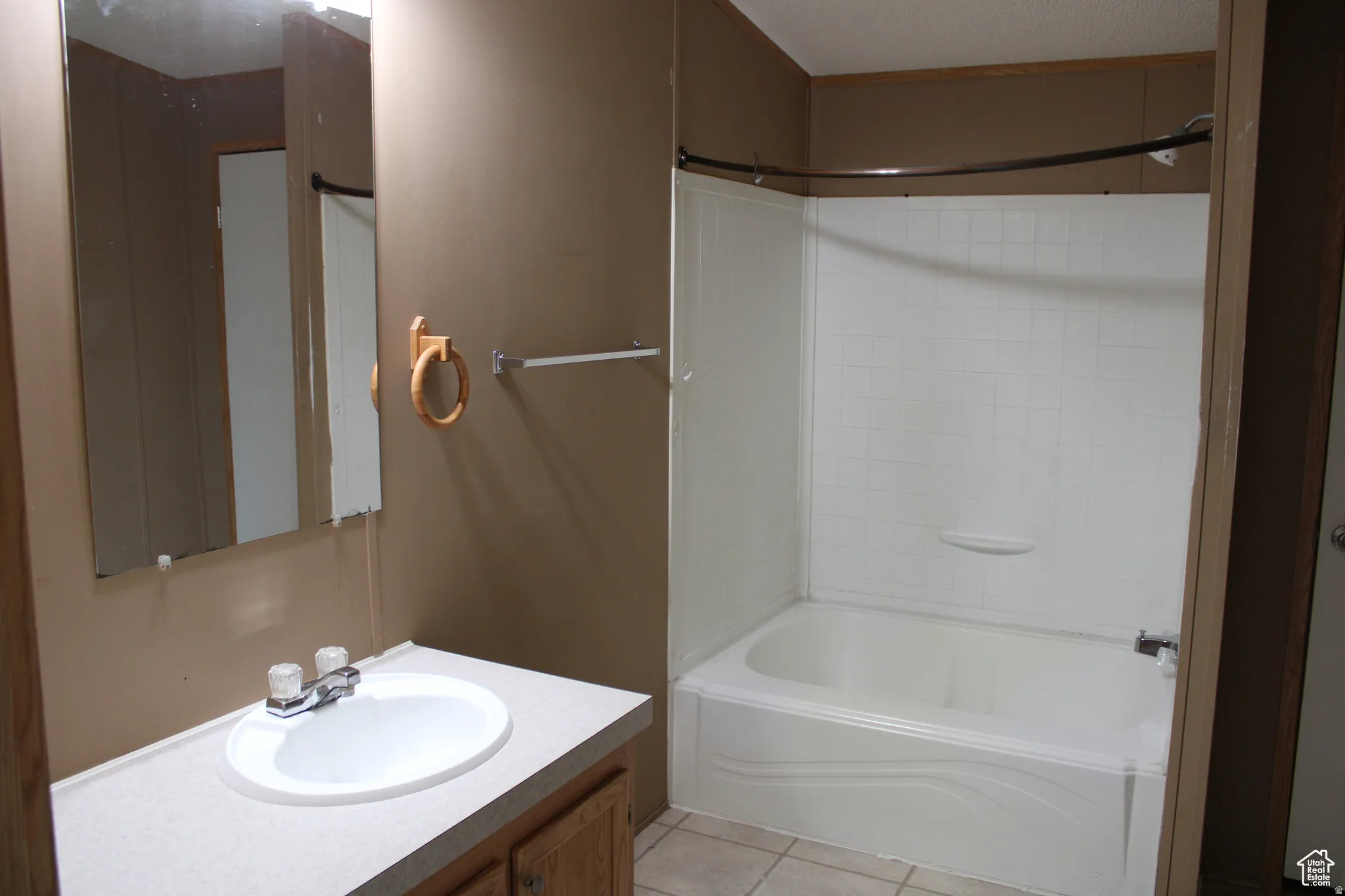 Bathroom featuring an integrated vanity sink with a laminate countertop, a large wall-mounted mirror, a tub/shower combination with white tiled walls, and a chrome faucet
