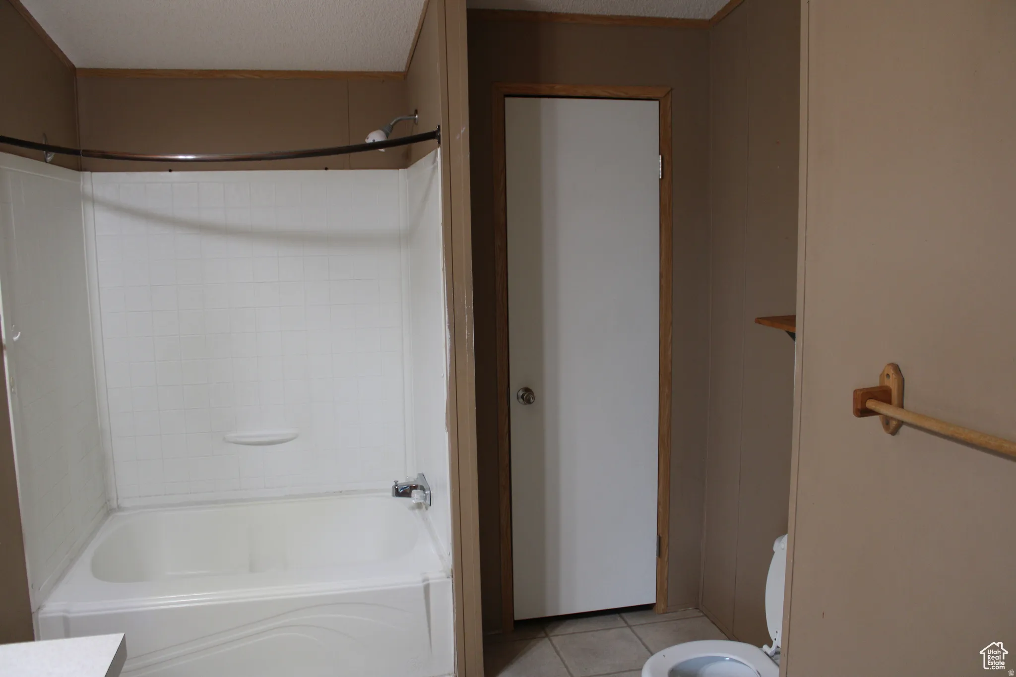 White tub and shower combination with chrome fixtures, surrounded by beige paneling and wood trim