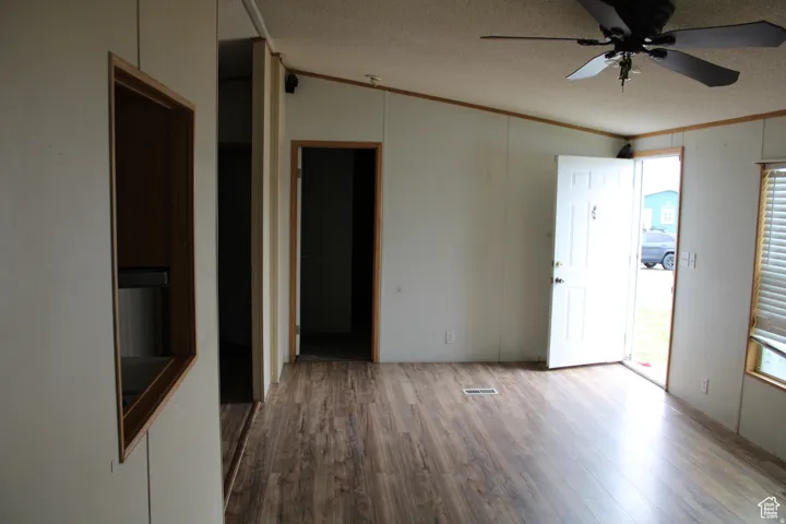Open living space featuring wood-finish flooring, a ceiling fan, and a front entry door with a window