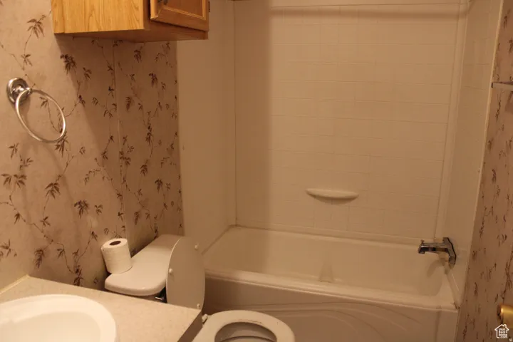 Full bathroom featuring a white bathtub with a tiled surround, a toilet, and a vanity with an integrated sink
