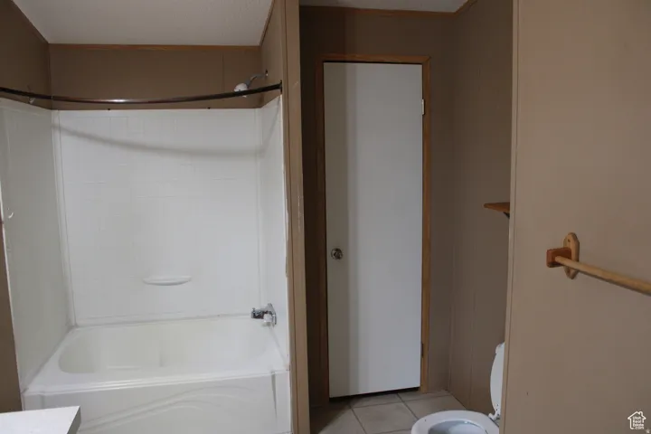 White tub and shower combination with chrome fixtures, surrounded by beige paneling and wood trim