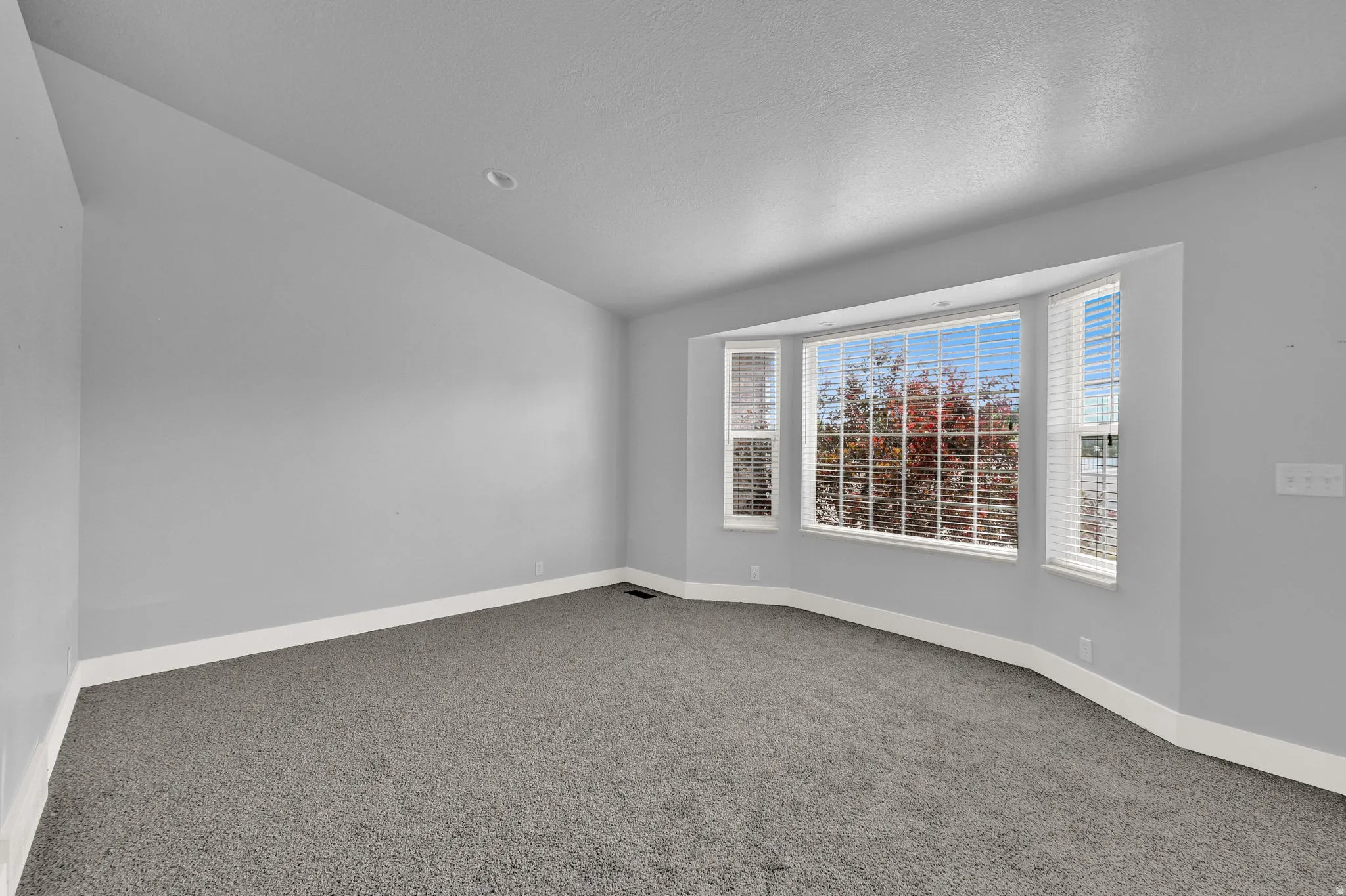 Spacious room featuring a bay window, gray carpeting, neutral wall paint, white baseboards, and recessed lighting