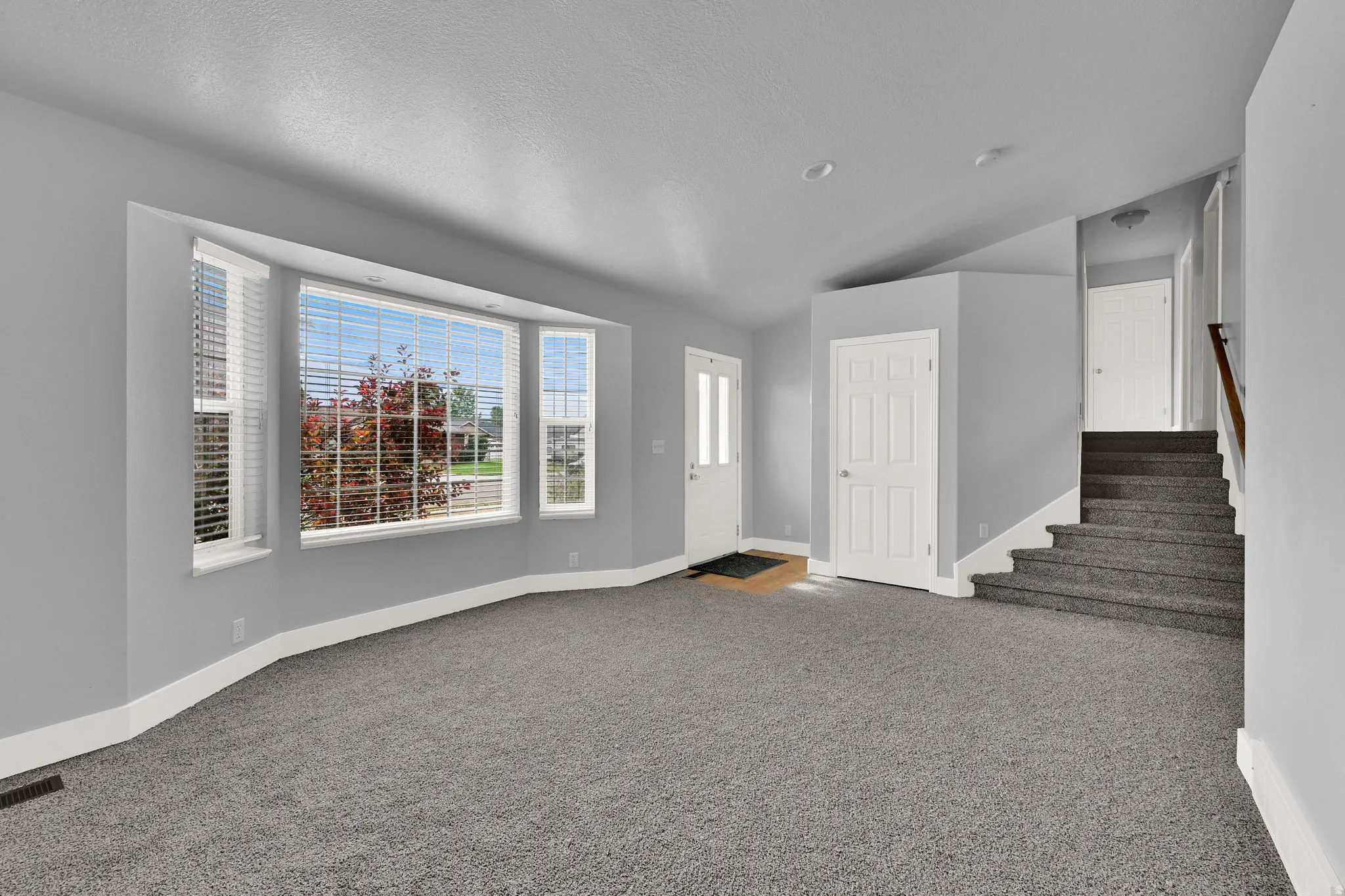 Spacious interior featuring a bay window, neutral gray walls, and plush gray carpeting