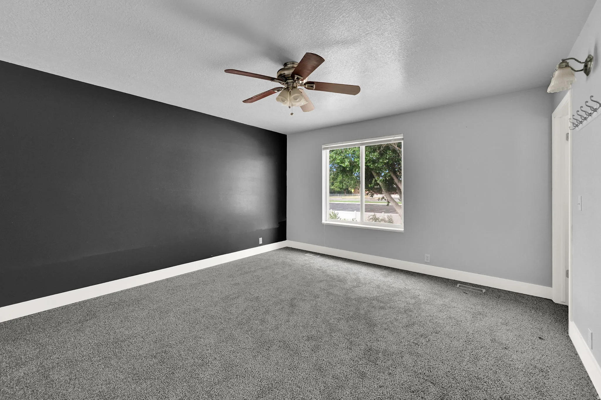 Spacious interior room featuring a large window, ceiling fan, and grey carpet