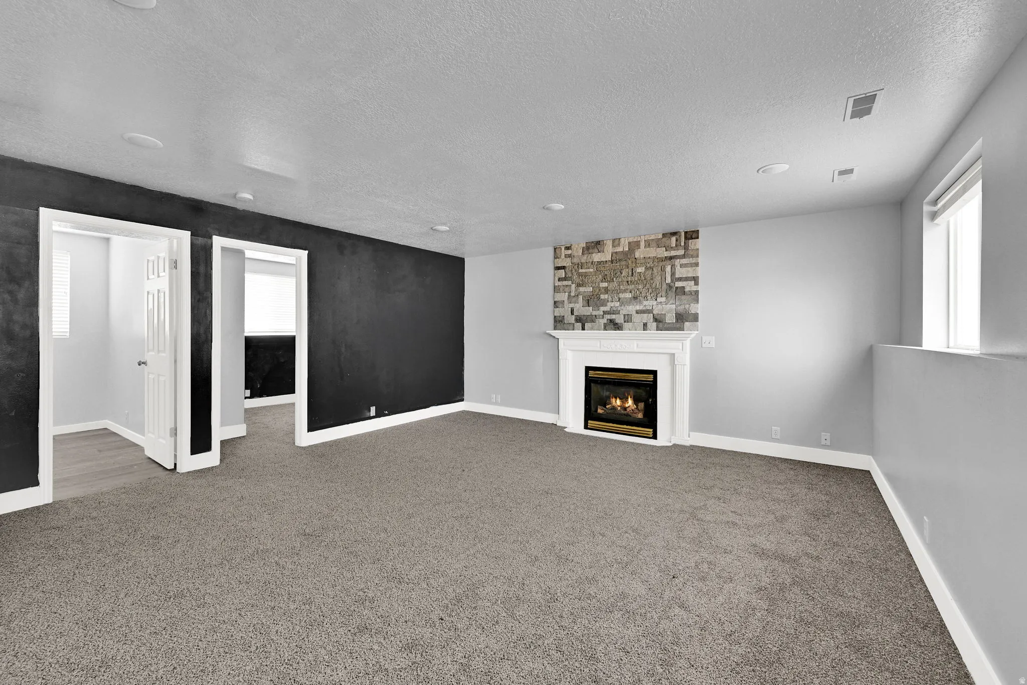 Spacious room featuring a white-mantled fireplace with a stone-look surround, recessed lighting, and grey carpet flooring