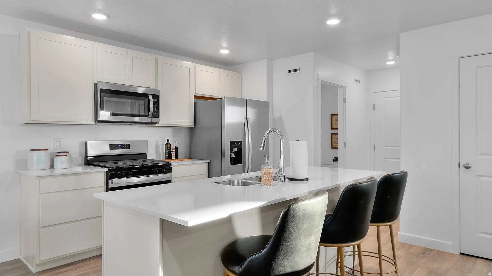 Modern kitchen featuring white shaker cabinetry, stainless steel appliances, a white solid surface countertop island with seating, recessed lighting, and wood-finish flooring