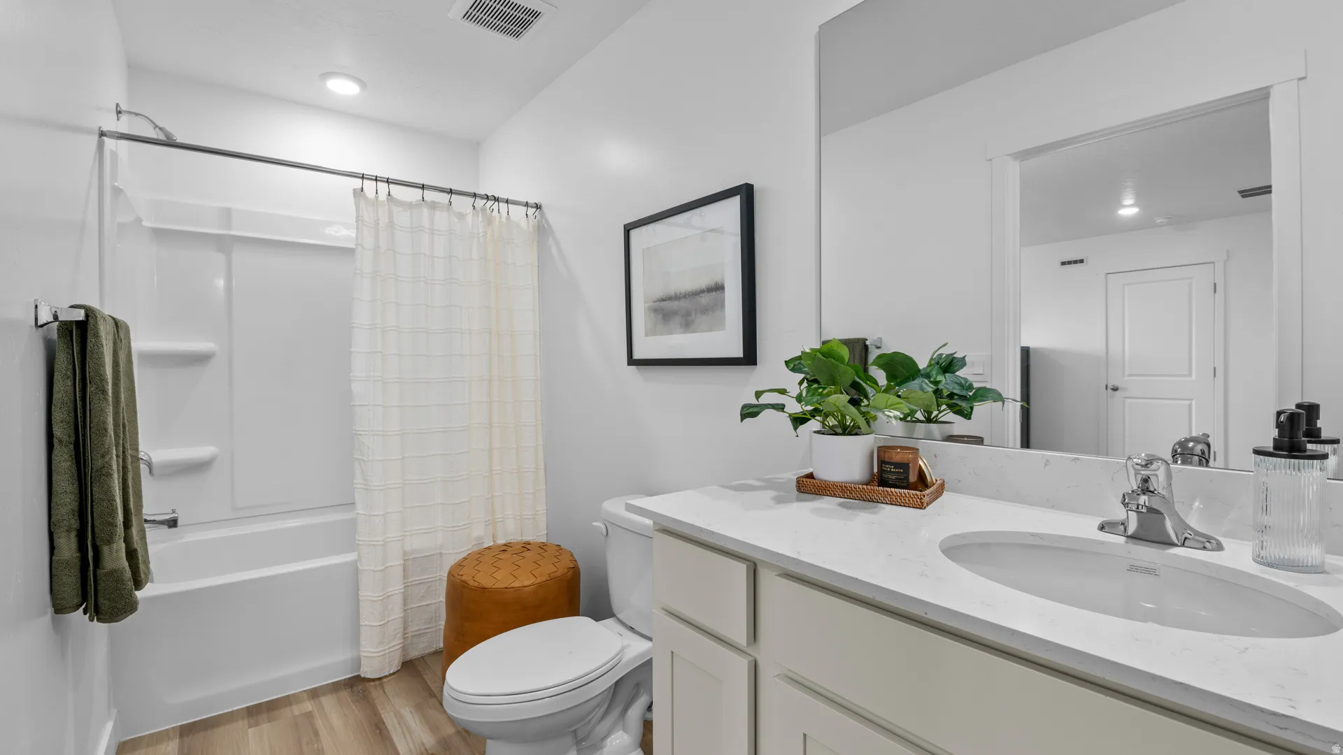 Bathroom featuring a white vanity with an integrated sink and chrome faucet, a large mirror, and a built-in tub with a shower