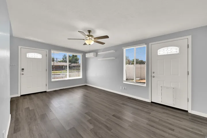 Spacious room featuring wood-finish flooring, light gray wall paint, and a ceiling fan with integrated lighting