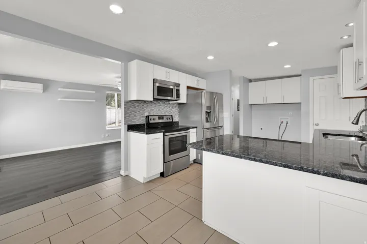 Kitchen featuring an island with a dark countertop, white cabinetry, stainless steel appliances, and a tiled backsplash